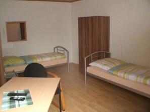A dormitory room with two single beds, a wooden desk, a chair, and a wardrobe. - Gästehaus Willis (Goslar)