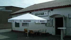 A small outdoor seating area with a white umbrella labeled "VELTINS" and a sign for "GASTSTÄTTE." - Gästehaus Willis (Goslar)