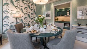 Un coin repas avec une table ronde, des chaises à revêtement gris, un vase avec des fleurs et un mur orné d’un motif de feuilles tropicales.