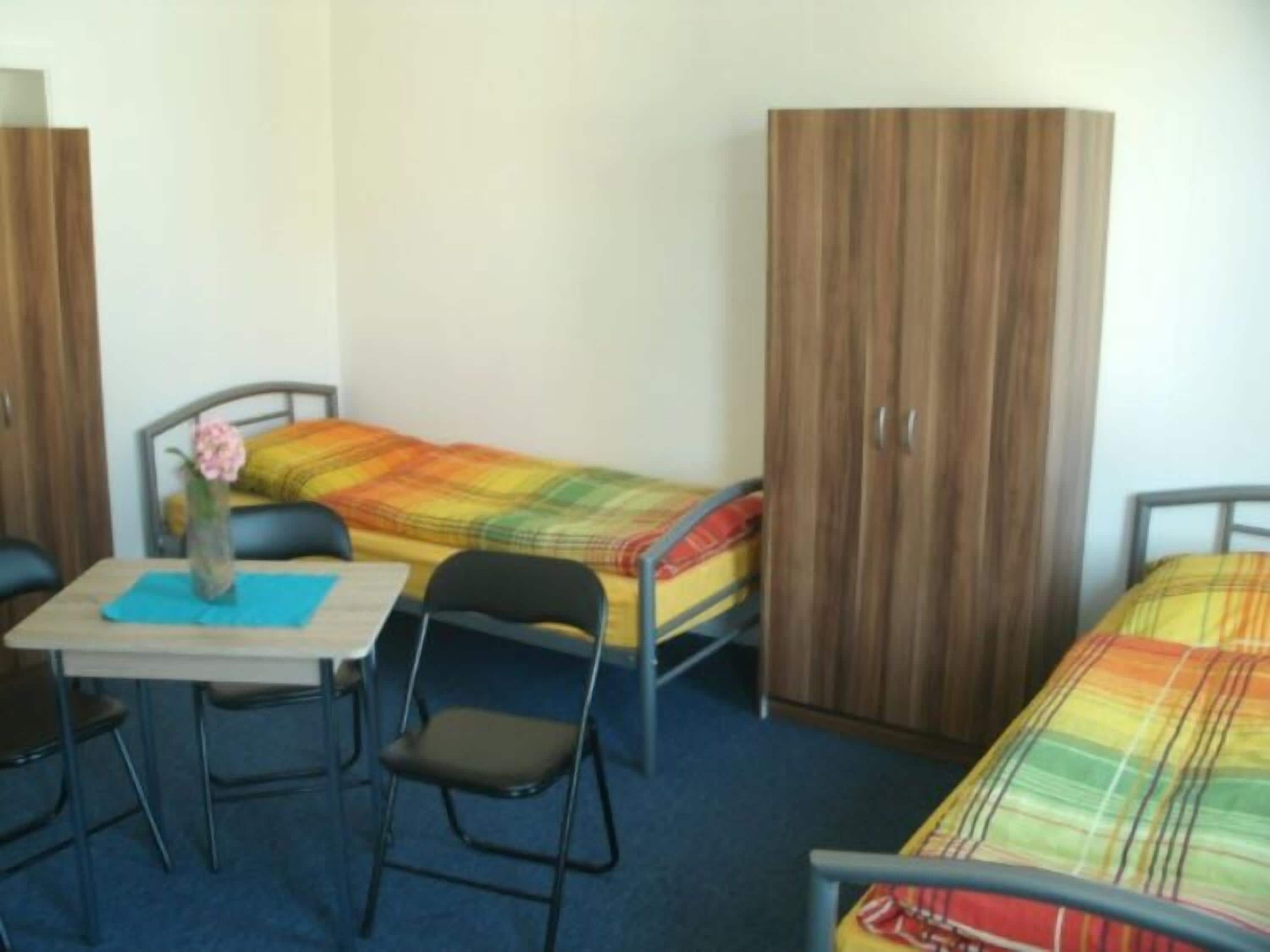 A small, single-room accommodation with a bed, a desk, a chair, and a wardrobe.