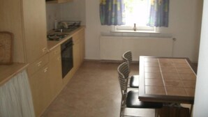 A small kitchen with wooden cabinets, a stove, a sink, and a window with curtains. - Gästehaus Harz (Goslar)