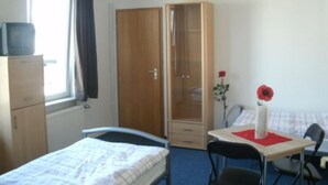 A room with a bed, a desk with a chair, a wardrobe, and a window with curtains. - Gästehaus Harz (Goslar)
