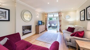 A living room with a fireplace, a television, and a sofa. There is a view of an outdoor patio with a table and chairs.