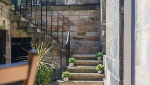 A stone staircase leading to a door, with potted plants on the steps and a chair in the foreground.