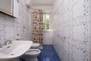 Une salle de bain avec un lavabo blanc, deux toilettes et un rideau de douche Ă motifs floraux.