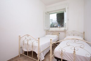 A room with two metal beds, a window with a view, and a white wall.