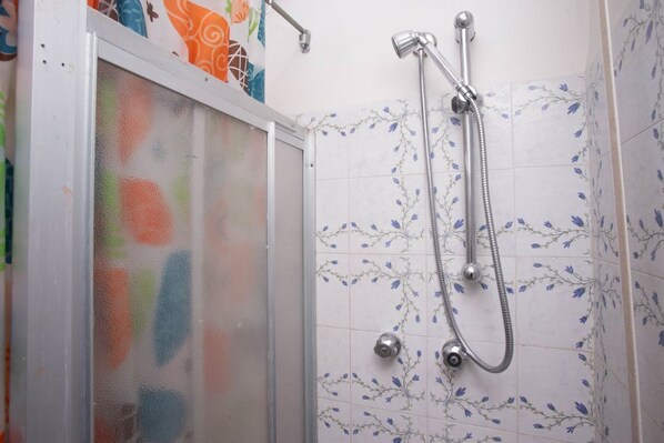 Ducha con cabezal de ducha manual y grifo empotrado en la pared, puerta de vidrio esmerilado y azulejos con estampado floral.