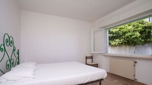 Een slaapkamer met een enkel bed, een stoel, een radiator en een raam met uitzicht op groen.