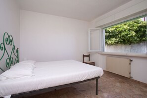 Une chambre avec un lit simple, une chaise, un radiateur et une fenĂȘtre donnant sur un espace verdoyant.