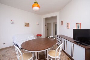 A dining area with a round table, white chairs, a TV, and a cabinet.