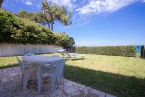 A patio with a table and chairs, a hedge, and a clear sky.