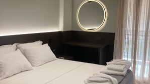 A modern hotel room with a neatly made bed, a round mirror, and a bedside table. - Amazing Beach Front Apartment in the Athens Riviera (Vouliagmeni)