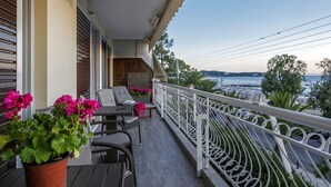 A balcony with wicker furniture, a potted plant, and a view of the sea. - Amazing Beach Front Apartment in the Athens Riviera (Vouliagmeni)