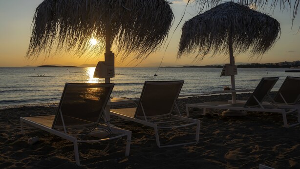 A beach with lounge chairs and thatched umbrellas, overlooking the sea at sunset. - Amazing Beach Front Apartment in the Athens Riviera (Vouliagmeni)