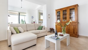 A living room with a beige sofa, a white coffee table with magazines, a wooden cabinet, and a vase with flowers. - Villa Sun Total Relax (Alcamo)