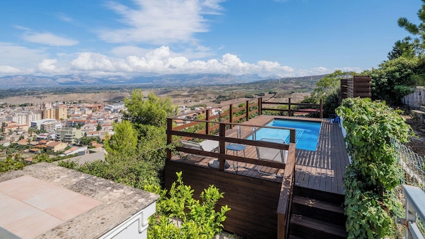 A rooftop pool with a wooden deck and a view of a cityscape and mountains in the background. - Villa Sun Total Relax (Alcamo)