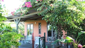 A covered outdoor area with a small building, a fenced patio, and lush greenery. - Gite des Acacias (Carreau Accacia)