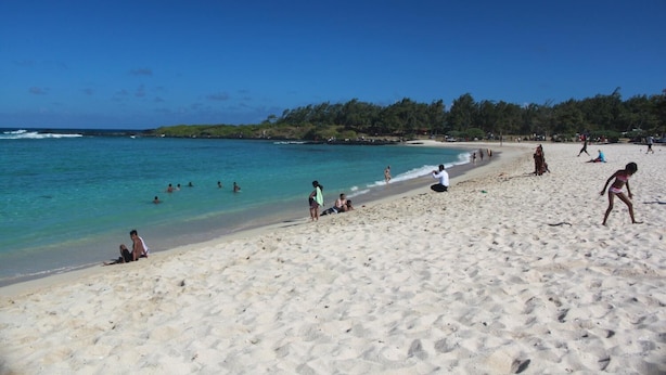 A beach with people swimming and walking along the shore. - Gite des Acacias (Carreau Accacia)