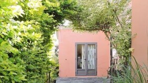 A pathway leading to a building with a door, surrounded by greenery and a gravel path. - Gite des Acacias (Carreau Accacia)