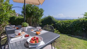 Uma área de refeições ao ar livre com uma mesa posta para dois, um guarda-sol bege e vista para a paisagem.