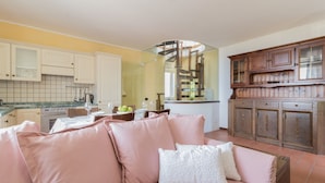 Cozinha moderna com armários brancos, área de jantar com sofá rosa e um aparador de madeira com portas de vidro.