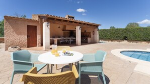 An outdoor patio with a round table and chairs, a pool, and a stone building with a tiled roof. - Can Pere Xine, Mallorcan Charm near Cala Mondragó (santañy)
