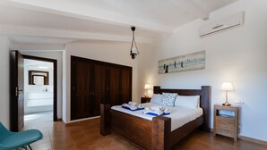 A bedroom with a wooden bed, bedside lamps, a nightstand, a blue chair, and a painting on the wall. - Can Pere Xine, Mallorcan Charm near Cala Mondragó (santañy)