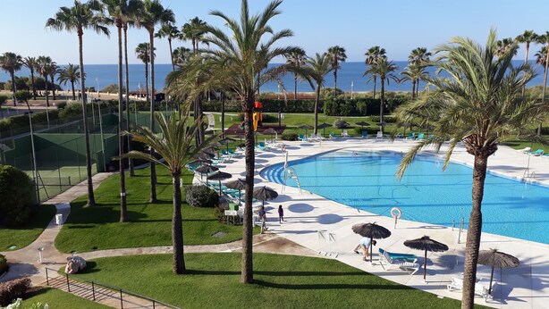 A resort pool area with palm trees, lounge chairs, and a clear view of the ocean. - Islantur Las Américas (Isla Cristina)