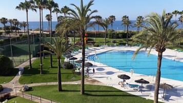 A resort pool area with palm trees, lounge chairs, and a clear view of the ocean.