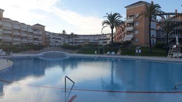 Una gran piscina con borde de piedra, rodeada por un edificio de varios pisos con balcones y palmeras.