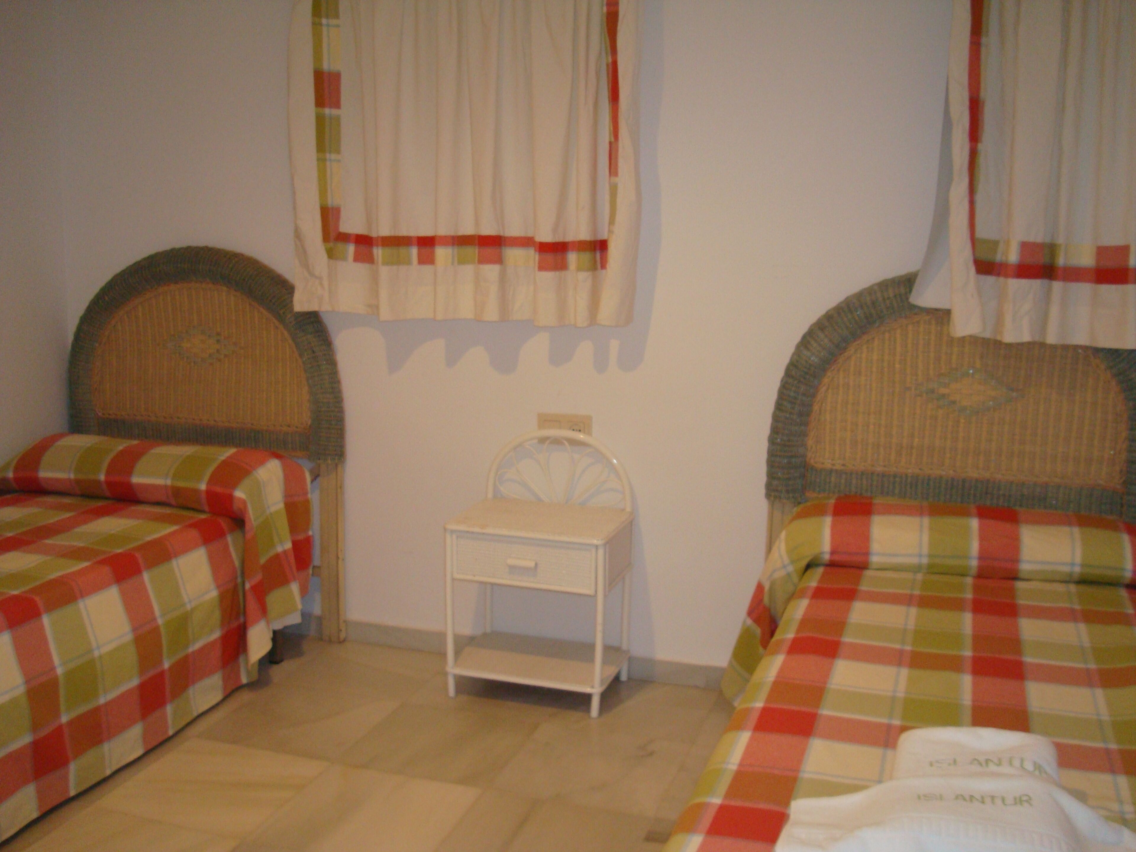 Un dormitorio con dos camas, cada una con una colcha a cuadros, una mesita de noche pequeña y una mesita auxiliar.