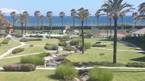 A landscaped garden with palm trees, a pool, and a tennis court. - Islantur Las Américas (Isla Cristina)