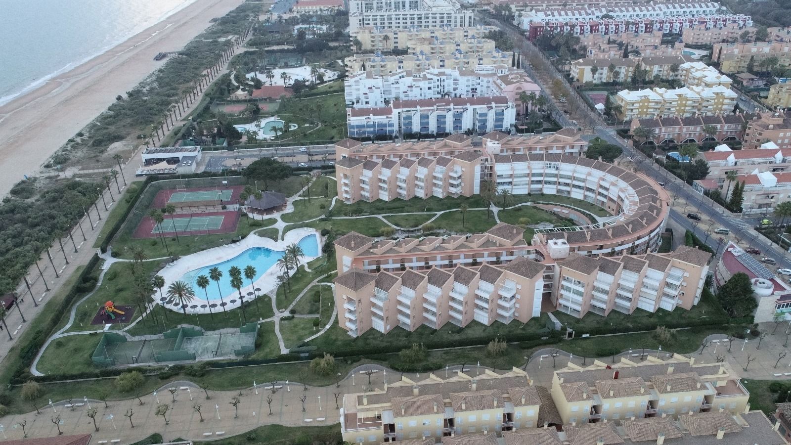 Vista aérea de un hotel costero con varias construcciones, piscina y jardines con senderos.