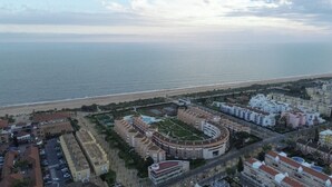 An aerial view of a coastal city with a large circular building complex, a beach, and surrounding residential areas. - Islantur Las Américas (Isla Cristina)