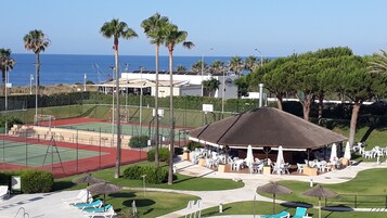 Una cancha deportiva con una pista de tenis, un pabellón y asientos exteriores con sombrillas.
