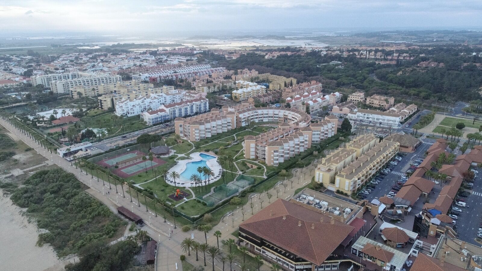 An aerial view of a residential area with multiple apartment buildings, a central swimming pool, and surrounding greenery.