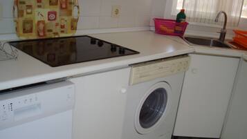 Cocina compacta con lavadora integrada, un lavamanos pequeño y una encimera con hervidor.