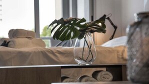 A bed with a beige cover, a clear vase with a plant, and a lamp on a bedside table.
