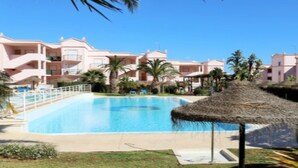 A swimming pool surrounded by a resort building with balconies and palm trees. - SAINT JAMES - APT SEA VIEW - 2 / 4PERS (Luz)