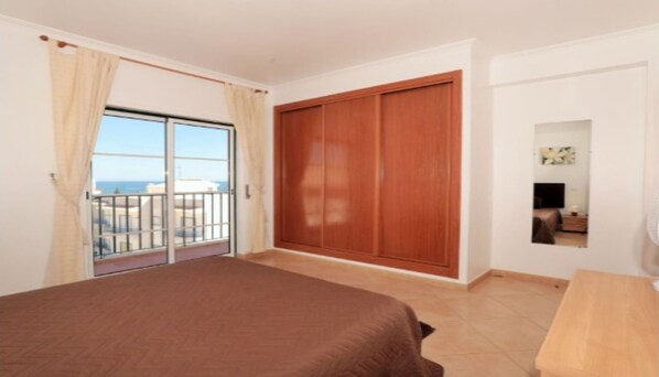 A bedroom with a large bed, a wooden wardrobe, a sliding glass door to a balcony, and a small table. - SAINT JAMES - APT SEA VIEW - 2 / 4PERS (Luz)