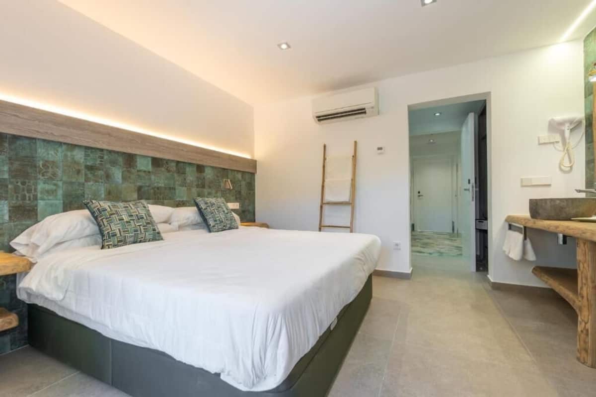 Un dormitorio moderno con una cama grande, un cabecero de madera, una mesita de noche y una banca empotrada con lavamanos.
