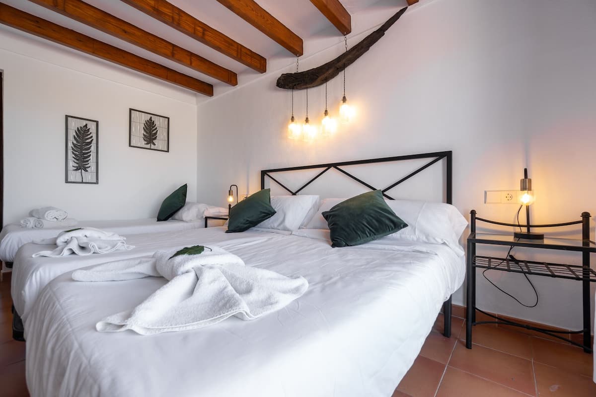 Habitación de hotel con dos camas, vigas de madera en el techo, obra de arte con forma de hojas en la pared y lámparas de noche.