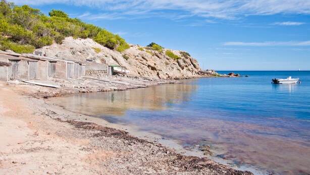 A coastal scene with a rocky shoreline, a small boat, and a clear sky. - Hostal Restaurante Pou Des Lleó (Santa Eulalia del Rio)