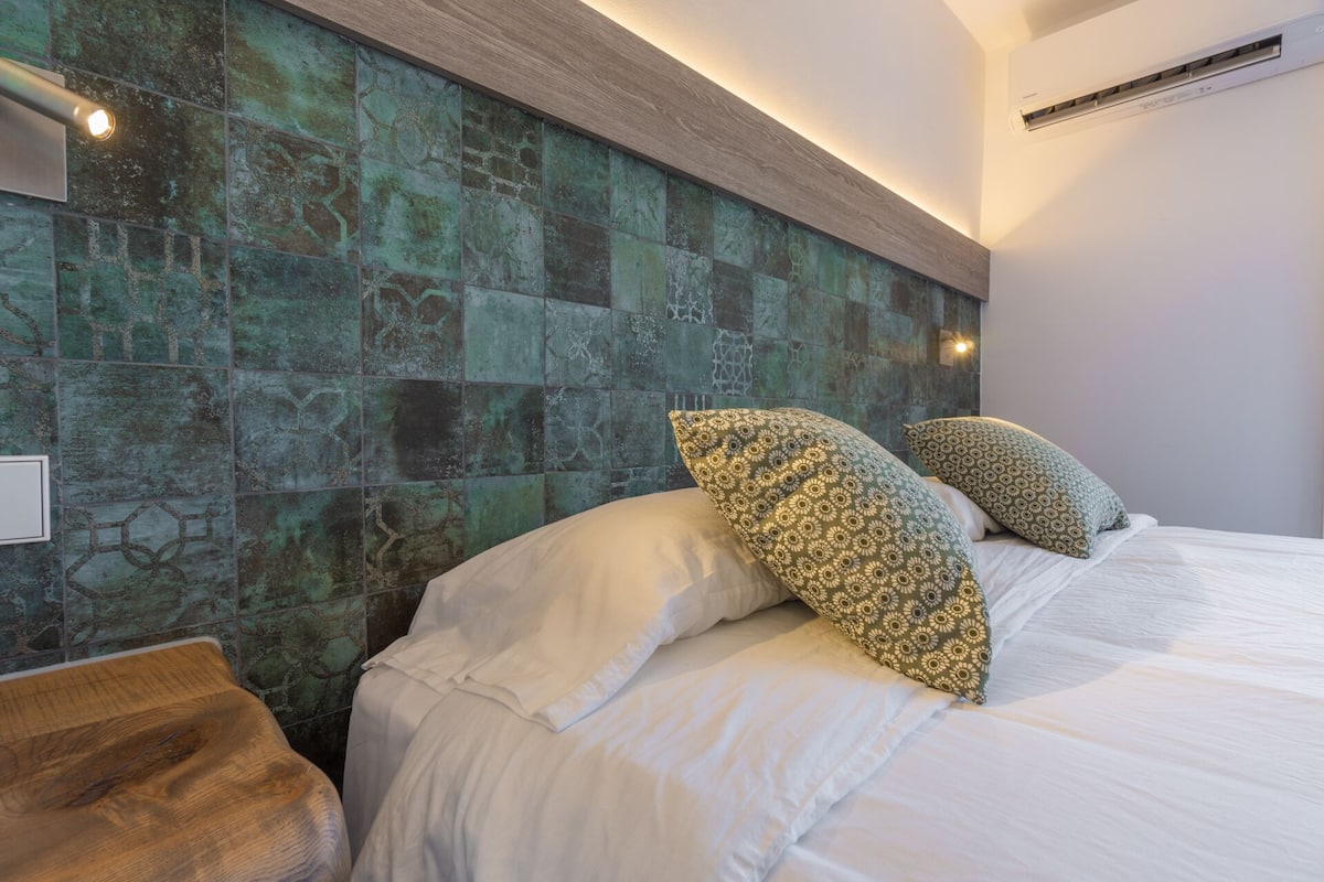Un dormitorio moderno con una cama grande, almohadas estampadas y una pared con textura.