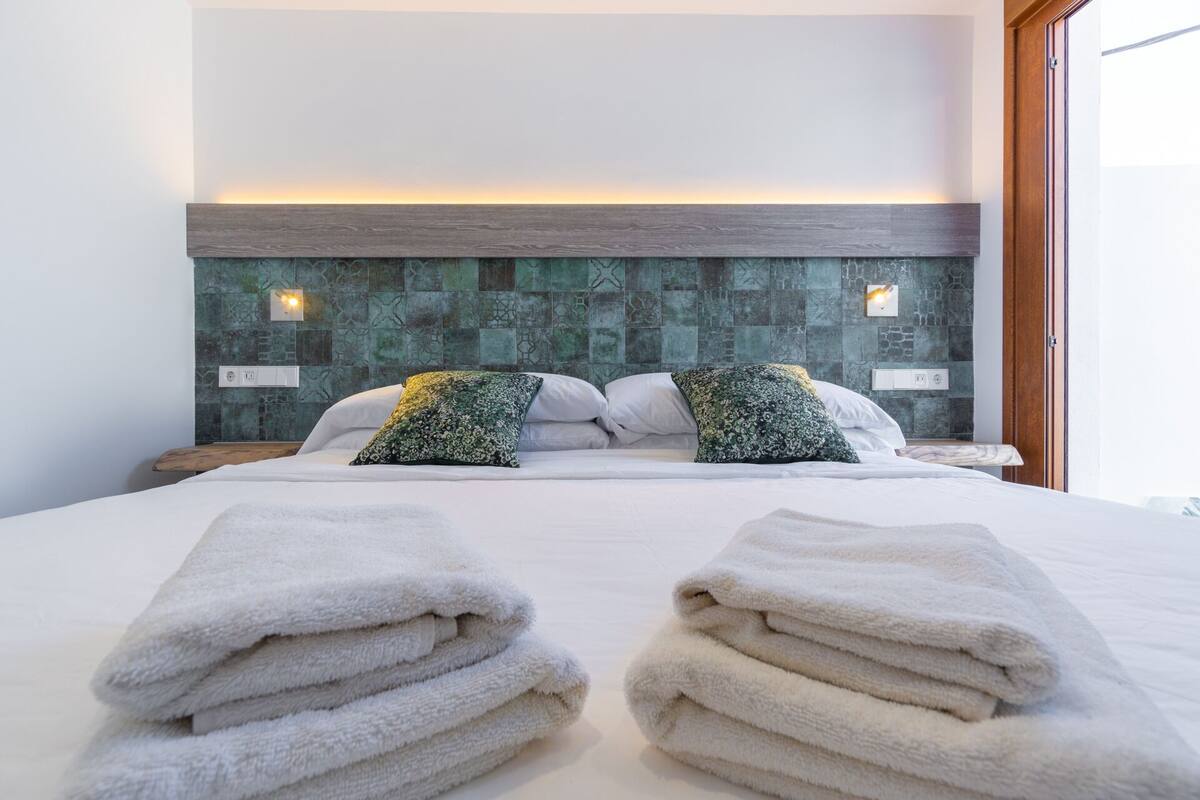 Cama bien hecha con dos almohadas y dos toallas dobladas al frente.