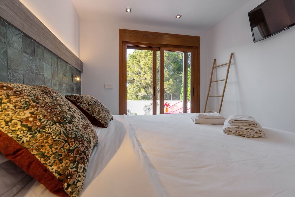 Un dormitorio con una cama grande, cabecera de madera, televisor montado en la pared y vistas al exterior a través de una puerta corredera.