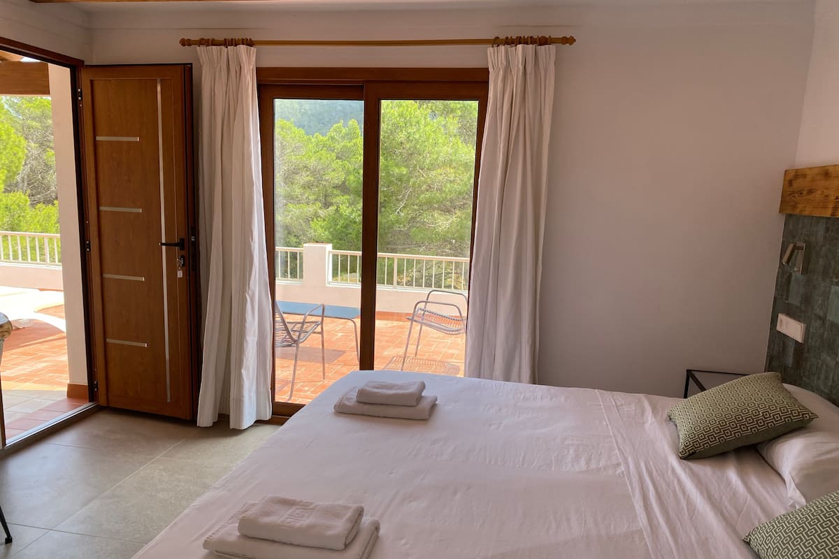 Un dormitorio con una cama grande, un balcón con sillas y una puerta de madera.