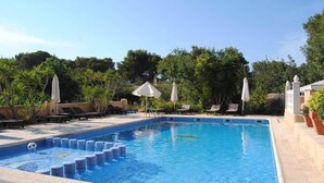 A rectangular swimming pool with blue tiles, surrounded by lounge chairs and umbrellas, set against a backdrop of trees and a clear sky. - Hostal Restaurante Pou Des Lleó (Santa Eulalia del Rio)