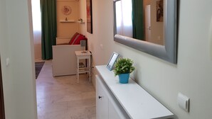 Uma sala de estar moderna com um sofá branco, uma mesinha de centro com abajur, uma planta azul em vaso e um espelho grande na parede.