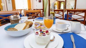 Una escena de desayuno con un tazón de cereal, un vaso de jugo de naranja, una taza de café y una jarra de leche sobre una mesa.